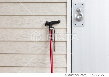 A walking stick leaning against the front door; a reflection of the daily life and lifestyle of a senior citizen. A walking stick leaning against the front door; a reflection of the daily life and lifestyle of a senior citizen. 142551270