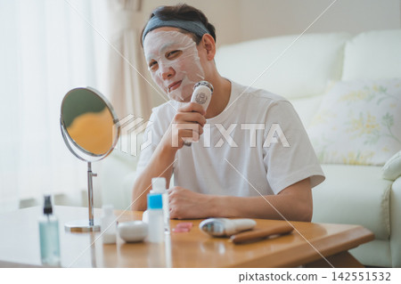 A 40-something man's beauty routine: using a facial mask while carefully caring for his cheeks with a facial device. 142551532