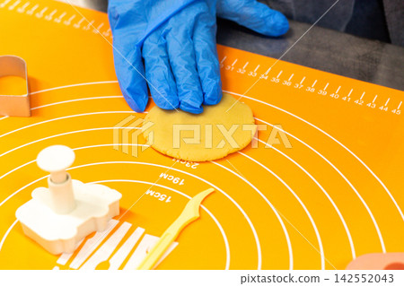 Hand in blue gloves creating shape of marzipan candy from dough using cookie cutter. Handmade marzipan sweets Hand in blue gloves creating shape of marzipan candy from dough using cookie cutter. Handmade marzipan sweets 142552043