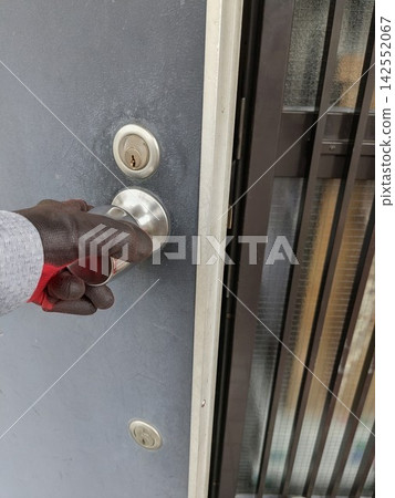 A burglar or suspicious person wearing gloves turns the doorknob of a detached house. A burglar or suspicious person wearing gloves turns the doorknob of a detached house. 142552067