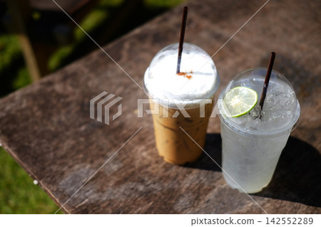 Top view of fresh iced latte coffee and Lime juice in plastic glass in wooden table outdoor in natural sunlight. Copy space Top view of fresh iced latte coffee and Lime juice in plastic glass in wooden table outdoor in natural sunlight. Copy space 142552289