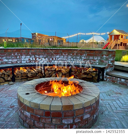 Outdoor fire pit glowing at dusk in cozy countryside resort with warm evening atmosphere Outdoor fire pit glowing at dusk in cozy countryside resort with warm evening atmosphere 142552355