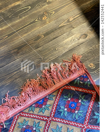 Traditional woven rug on dark wooden floor with rustic texture and ethnic pattern Traditional woven rug on dark wooden floor with rustic texture and ethnic pattern 142552441