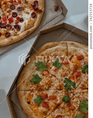 Two Fresh Pizzas in Cardboard Boxes on White Table Two Fresh Pizzas in Cardboard Boxes on White Table 142553719