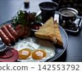 Closeup fried eggs in sunny side up style served with toast and ham with blurred background of hot coffee cup 142553792