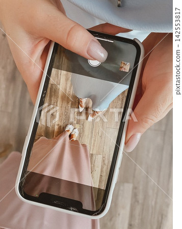 Woman photographing elegant outfit on smartphone during stylish indoor celebration 142553817