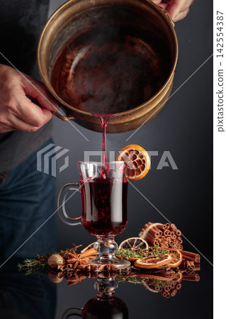 Mulled wine is poured from a old brass pan into a glass mug. Mulled wine is poured from a old brass pan into a glass mug. 142554387