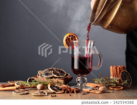 Mulled wine is poured from a old brass pan into a glass mug. Mulled wine is poured from a old brass pan into a glass mug. 142554388