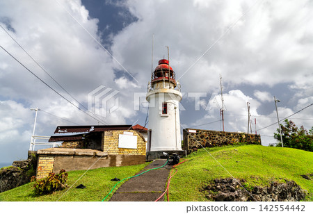 Historic Vigie Lighthouse standing on a grassy hill against a cloudy sky in Castries, Saint Lucia. Historic Vigie Lighthouse standing on a grassy hill against a cloudy sky in Castries, Saint Lucia. 142554442