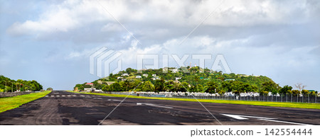 Asphalt runway and surrounding green hills at George F. L. Charles Airport in Castries, Saint Lucia under a cloudy sky. Asphalt runway and surrounding green hills at George F. L. Charles Airport in Castries, Saint Lucia under a cloudy sky. 142554444