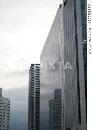 陰雲密佈的天空透過建築物的峽谷若隱若現。 陰雲密佈的天空透過建築物的峽谷若隱若現。 142554579