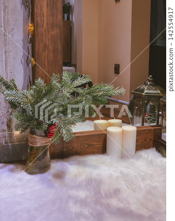 Cozy winter decor with pine branches and candles near mirror, warm interior scene Cozy winter decor with pine branches and candles near mirror, warm interior scene 142554917