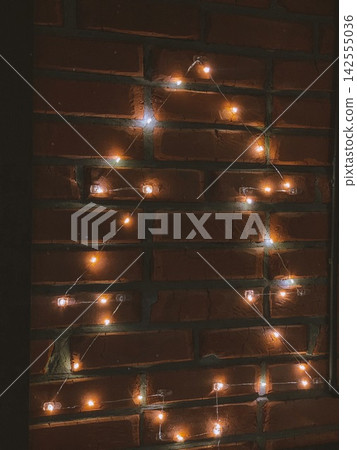Warm Christmas fairy lights on brick wall creating cozy festive minimal background Warm Christmas fairy lights on brick wall creating cozy festive minimal background 142555036