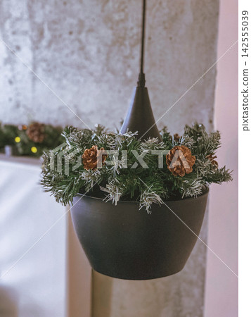 Minimalist Christmas decor with pine garland and pinecones on modern black hanging lamp Minimalist Christmas decor with pine garland and pinecones on modern black hanging lamp 142555039