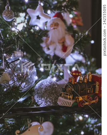 Christmas toy train on tree with festive lights and decorations, cozy holiday atmosphere Christmas toy train on tree with festive lights and decorations, cozy holiday atmosphere 142555095