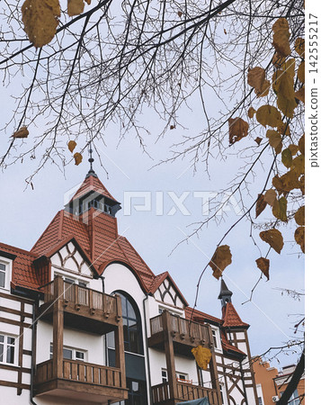 Charming European style building with red tiled roof and wooden balconies framed by autumn branches Charming European style building with red tiled roof and wooden balconies framed by autumn branches 142555217