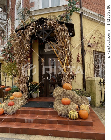Cozy autumn cafe entrance decorated with pumpkins, hay bales and dried corn for seasonal harvest festival Cozy autumn cafe entrance decorated with pumpkins, hay bales and dried corn for seasonal harvest festival 142555386