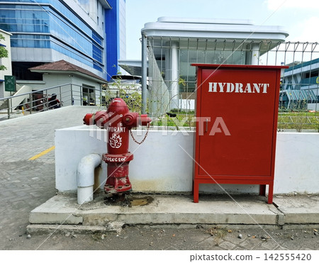 Red outdoor fire hydrant and storage box standing on concrete base near modern buildings. 142555420