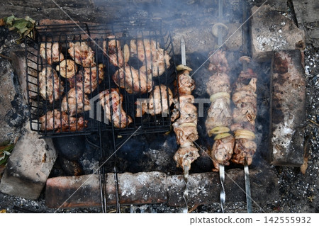 Smiling man flipping burgers on a gas grill at a backyard barbecue party. Summer outdoor cooking and social gathering concept. Man in apron grilling meat Smiling man flipping burgers on a gas grill at a backyard barbecue party. Summer outdoor cooking and social gathering concept. Man in apron grilling meat 142555932