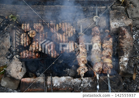 Smiling man flipping burgers on a gas grill at a backyard barbecue party. Summer outdoor cooking and social gathering concept. Man in apron grilling Smiling man flipping burgers on a gas grill at a backyard barbecue party. Summer outdoor cooking and social gathering concept. Man in apron grilling 142555937