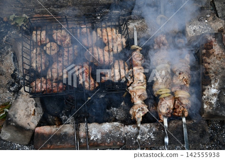 Smiling man flipping burgers on a gas grill at a backyard barbecue party. Summer outdoor cooking and social gathering concept. Man in apron grilling Smiling man flipping burgers on a gas grill at a backyard barbecue party. Summer outdoor cooking and social gathering concept. Man in apron grilling 142555938