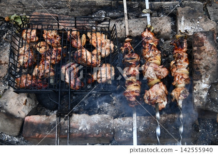 Smiling man flipping burgers on a gas grill at a backyard barbecue party. Summer outdoor cooking and social gathering concept. Man in apron grilling Smiling man flipping burgers on a gas grill at a backyard barbecue party. Summer outdoor cooking and social gathering concept. Man in apron grilling 142555940