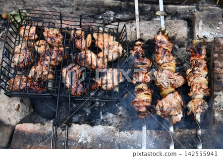 Smiling man flipping burgers on a gas grill at a backyard barbecue party. Summer outdoor cooking and social gathering concept. Man in apron grilling Smiling man flipping burgers on a gas grill at a backyard barbecue party. Summer outdoor cooking and social gathering concept. Man in apron grilling 142555941