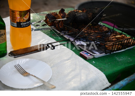 Smiling man flipping burgers on a gas grill at a backyard barbecue party. Summer outdoor cooking and social gathering concept. Man in apron grilling Smiling man flipping burgers on a gas grill at a backyard barbecue party. Summer outdoor cooking and social gathering concept. Man in apron grilling 142555947