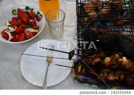 Smiling man flipping burgers on a gas grill at a backyard barbecue party. Summer outdoor cooking and social gathering concept. Man in apron grilling Smiling man flipping burgers on a gas grill at a backyard barbecue party. Summer outdoor cooking and social gathering concept. Man in apron grilling 142555948