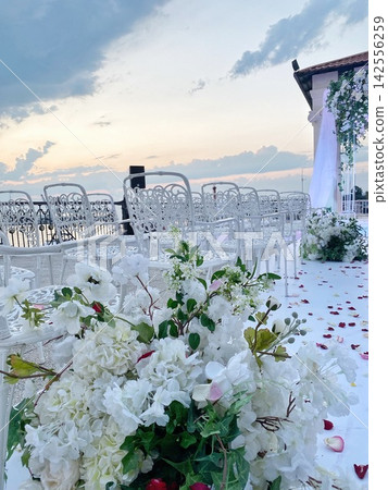 Wedding ceremony setup with flowers and chairs by sea, sunset light, romantic atmosphere Wedding ceremony setup with flowers and chairs by sea, sunset light, romantic atmosphere 142556259
