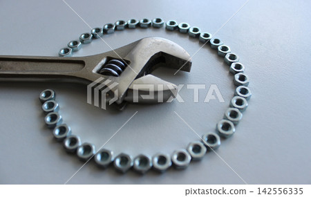 The spread jaws of an adjustable wrench are surrounded by a perfect circle of metal nuts The spread jaws of an adjustable wrench are surrounded by a perfect circle of metal nuts 142556335