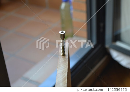 Closeup screw in wooden plank by glass door for diy carpentry background and home repair detail Closeup screw in wooden plank by glass door for diy carpentry background and home repair detail 142556353