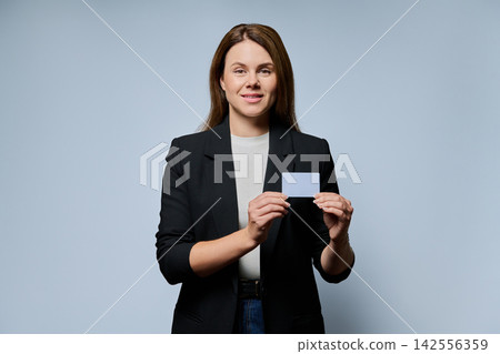 Adult businesswoman holding plastic credit card looking at camera on grey background Adult businesswoman holding plastic credit card looking at camera on grey background 142556359