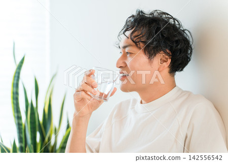 一位神采奕奕的男士在家喝水補充水分。 一位神采奕奕的男士在家喝水補充水分。 142556542