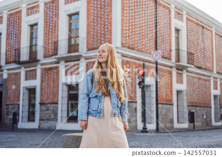 Woman tourist in a light dress and denim jacket walking through colorful colonial streets in Puebla Mexico with red brick building cobblestone road backpack solo female travel city break. Woman tourist in a light dress and denim jacket walking through colorful colonial streets in Puebla Mexico with red brick building cobblestone road backpack solo female travel city break. 142557031