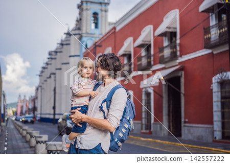 Father carrying his little son traveling near Puebla Cathedral and colonial red buildings in Puebla Mexico with family vacation street scene parenthood travel with children bonding moment. 142557222