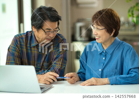 一對老年夫婦一邊看著電腦一邊輸入信用卡資訊。 一對老年夫婦一邊看著電腦一邊輸入信用卡資訊。 142557668