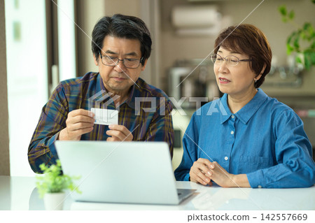 一對老年夫婦一邊看著電腦一邊輸入信用卡資訊。 142557669