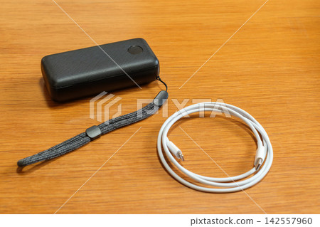 A mobile battery and charging cable placed on a wooden table: Image for disaster preparedness and power outage countermeasures. A mobile battery and charging cable placed on a wooden table: Image for disaster preparedness and power outage countermeasures. 142557960