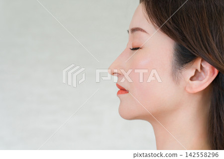 A close-up of the profile of a woman in her 40s, whose nose bridge and well-defined jawline are striking. A close-up of the profile of a woman in her 40s, whose nose bridge and well-defined jawline are striking. 142558296