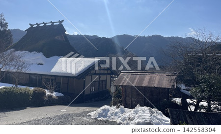 A snow-covered thatched-roof old farmhouse and a winter mountain village. A snow-covered thatched-roof old farmhouse and a winter mountain village. 142558304