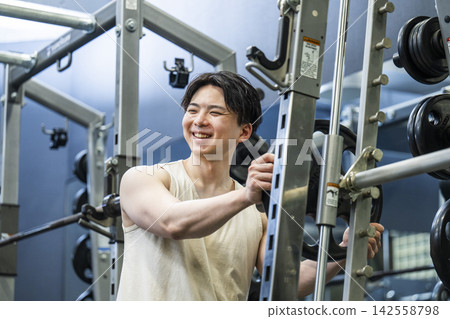 A young man sets a weight plate on a Smith machine. 142558798