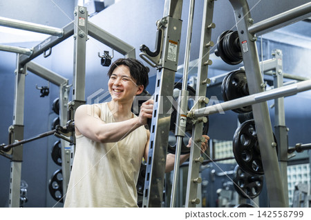 A young man sets a weight plate on a Smith machine. A young man sets a weight plate on a Smith machine. 142558799