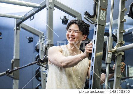 A young man sets a weight plate on a Smith machine. A young man sets a weight plate on a Smith machine. 142558800