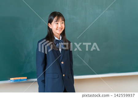 一位身穿校服的女學生在教室黑板前微笑。這幅教育材料讓人聯想到校園生活和新學年的開始。 一位身穿校服的女學生在教室黑板前微笑。這幅教育材料讓人聯想到校園生活和新學年的開始。 142559937