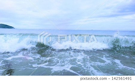 在陰雲密佈的天空下,湘南海的白色波浪和綿延的地平線構成了一幅美麗的景象。 在陰雲密佈的天空下,湘南海的白色波浪和綿延的地平線構成了一幅美麗的景象。 142561491