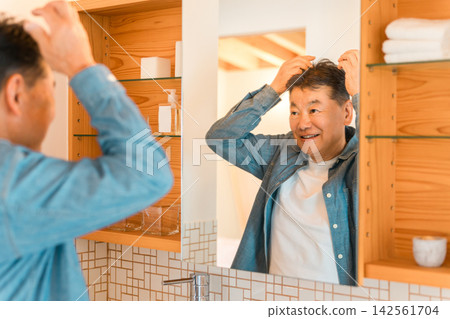 六、七十歲的老年男性在照鏡子時會檢查自己的頭髮和頭皮狀況。他們關心頭髮稀疏、脫髮、雄性禿（AGA）以及如何促進頭髮生長。 142561704