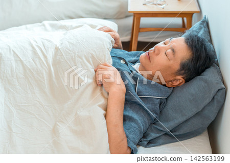 A senior man in his 60s or 70s sleeping on his back in his bed at home. An image related to sleep and health management. A senior man in his 60s or 70s sleeping on his back in his bed at home. An image related to sleep and health management. 142563199