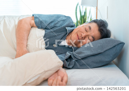 A senior man in his 60s or 70s sleeping in his bed at home. A bedroom lifestyle that evokes sleep, health, and restful sleep. A senior man in his 60s or 70s sleeping in his bed at home. A bedroom lifestyle that evokes sleep, health, and restful sleep. 142563201