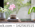 White ceramic cup on a notebook and tablet on wooden table 142563515